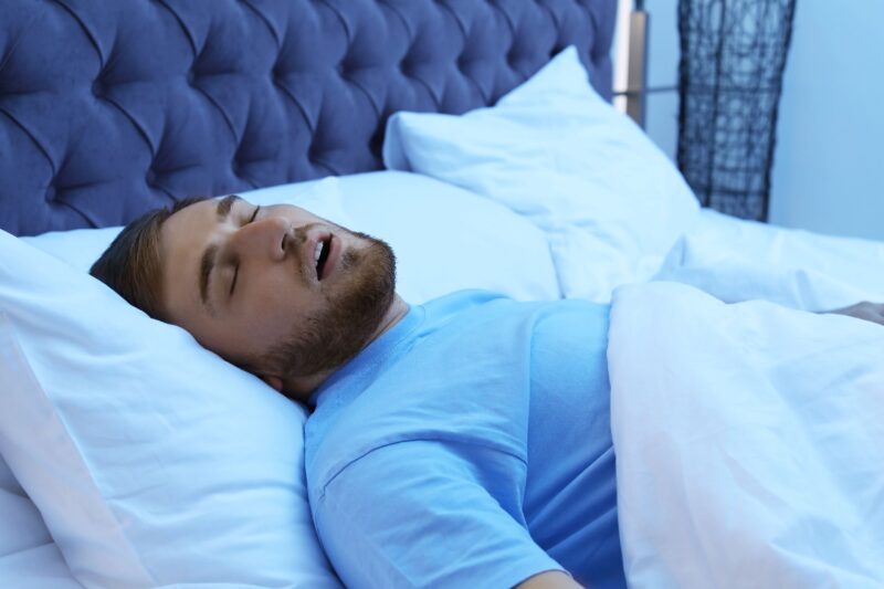 Man snoozing in bed with white sheets.
