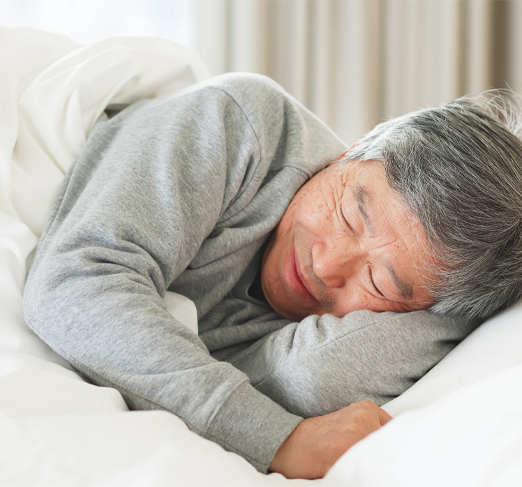 Senior man cuddling pillow while sleeping.
